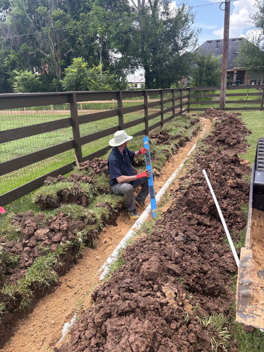 Crew leveling drain pipe by hand in a fresh trench — Richmond, TX